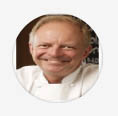 old smiling man wearing white chef coat with black background